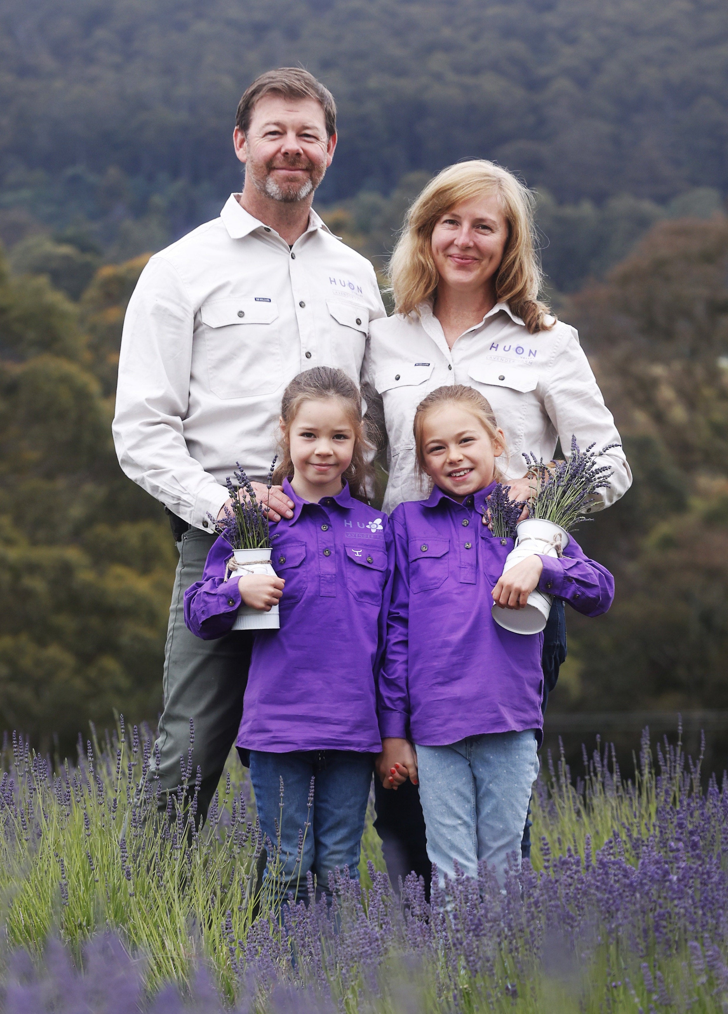 Family of four standing in a lavender field with trees in the background